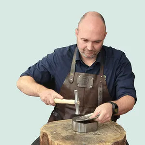 Goudsmid Remco Dijkstra met leren schort en hamer aan een houten blok